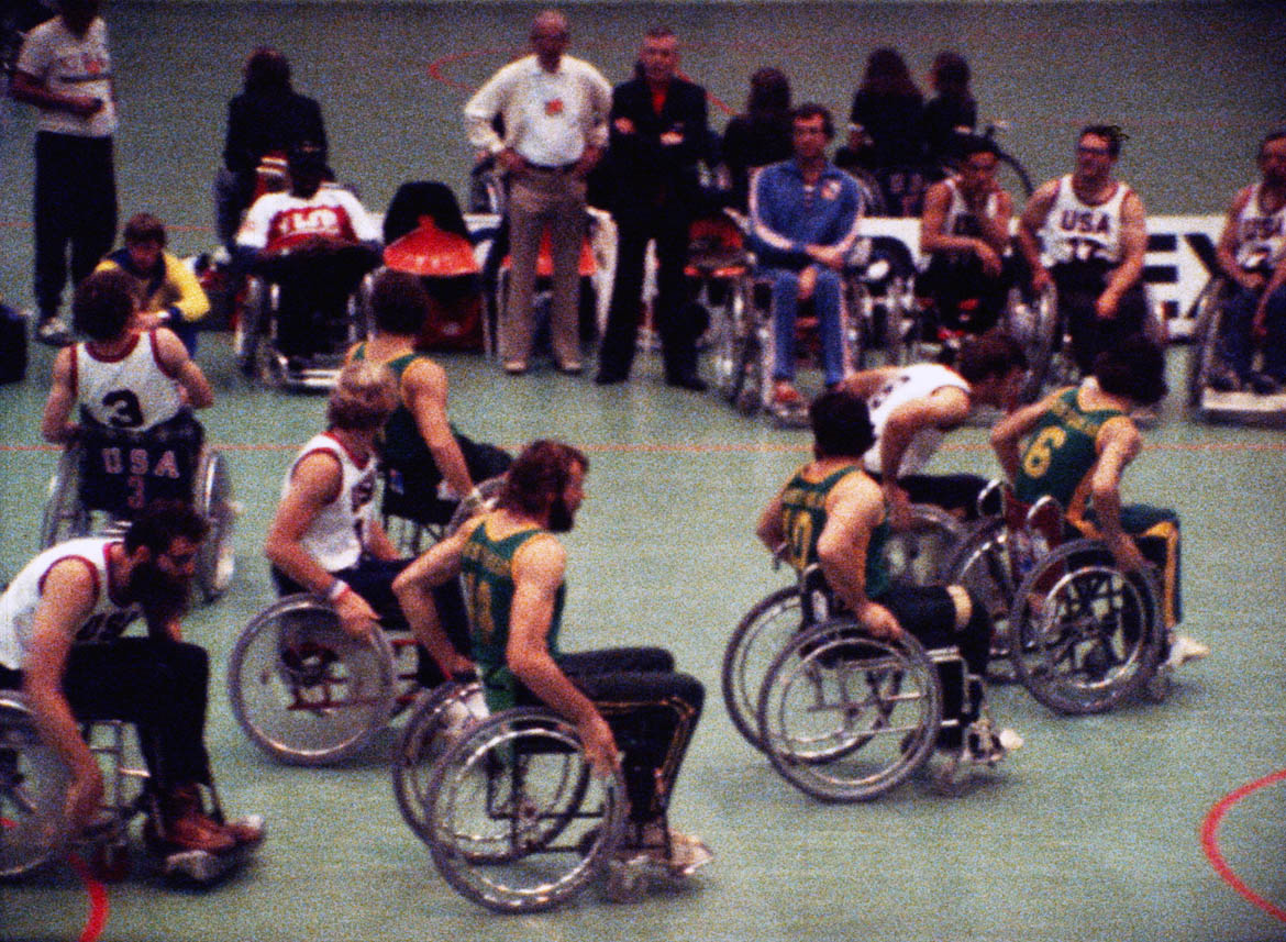 A moment from the game between the Australian and USA in wheelchair basketball at the 1980 summer Paralympics shows the stage of evolution of basketball chairs in 1980. The USA won easily, 87-36.This image is a still from a film made by Donald Worley about Australia's participation at the 1980 Summer Paralympics in Arnhem, Netherlands.
