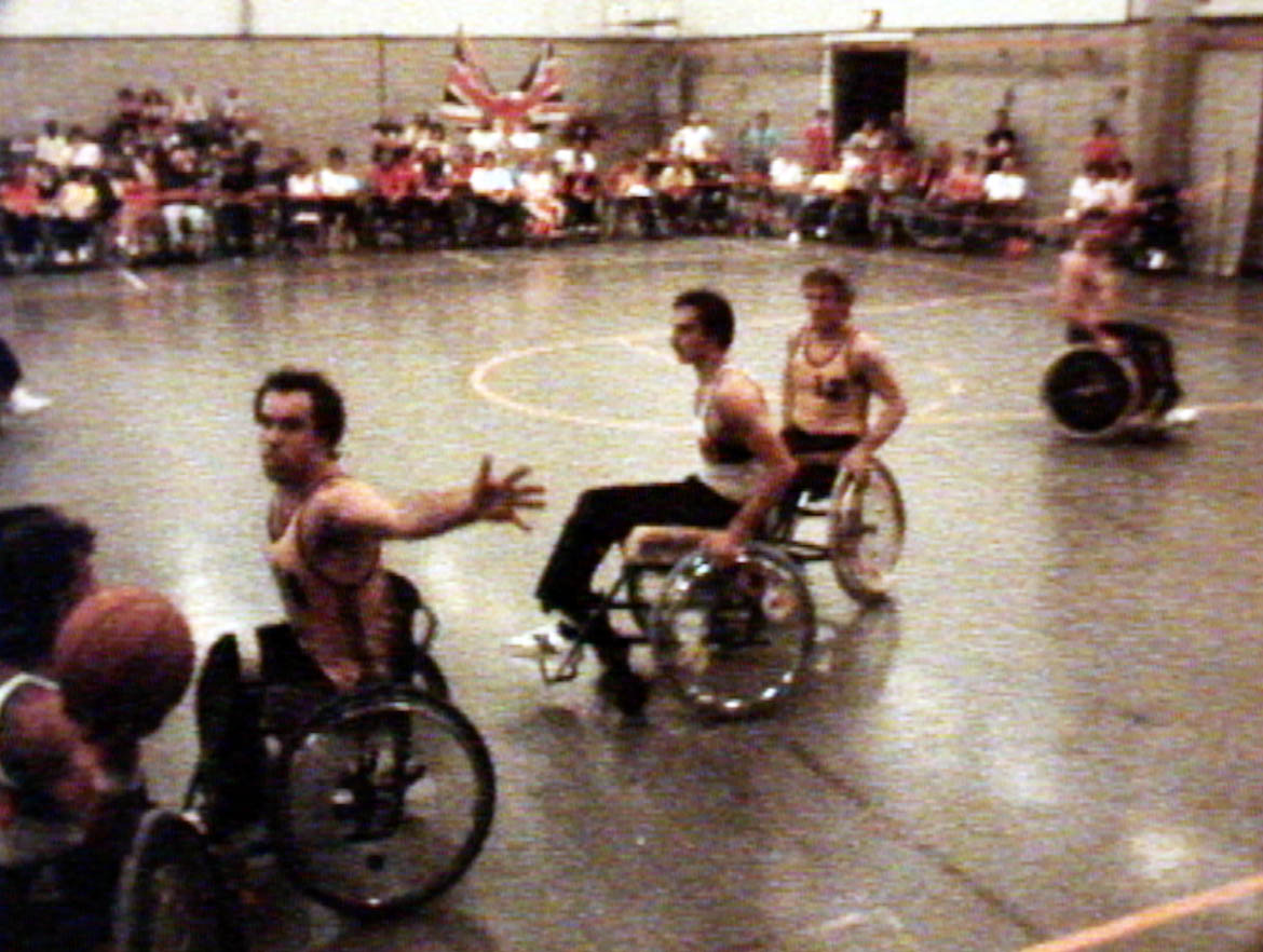 A scene for the wheelchair basketball game between Australian and Great Britain at the 1984 summer Paralympics. Great Britain won the game. This image is a still from a film made by Donald Worley about Australia's participation at the 1984 Summer Paralympics in Stoke Mandeville, England.